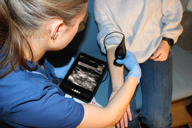 Nurse using a handheld ultrasound device connected to a tablet to examine a patient's arm during a home visit